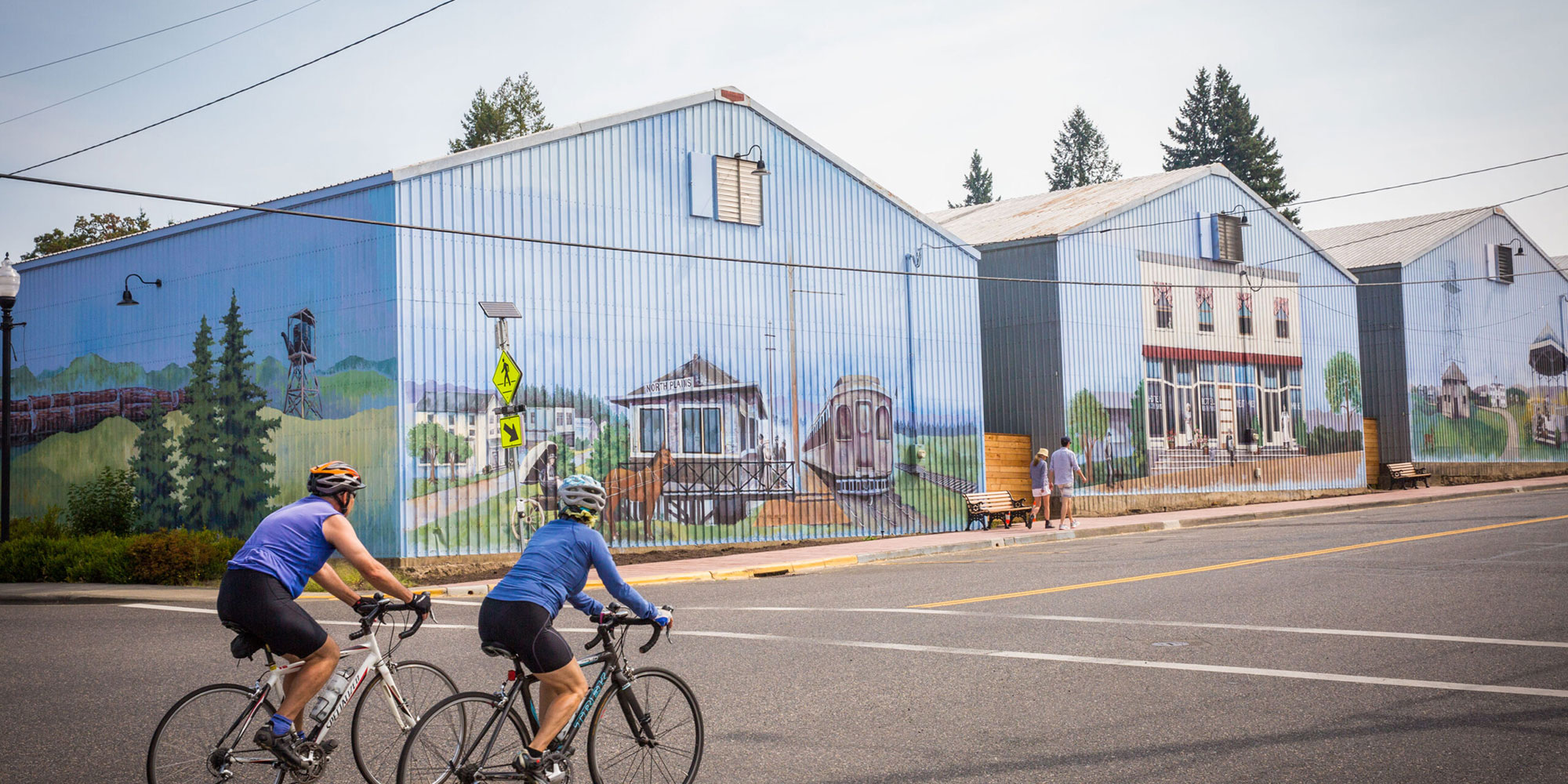 couple riding bike through North Plains admiring the murals