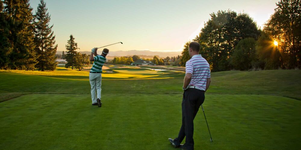 two golfers driving from a tee at sunset